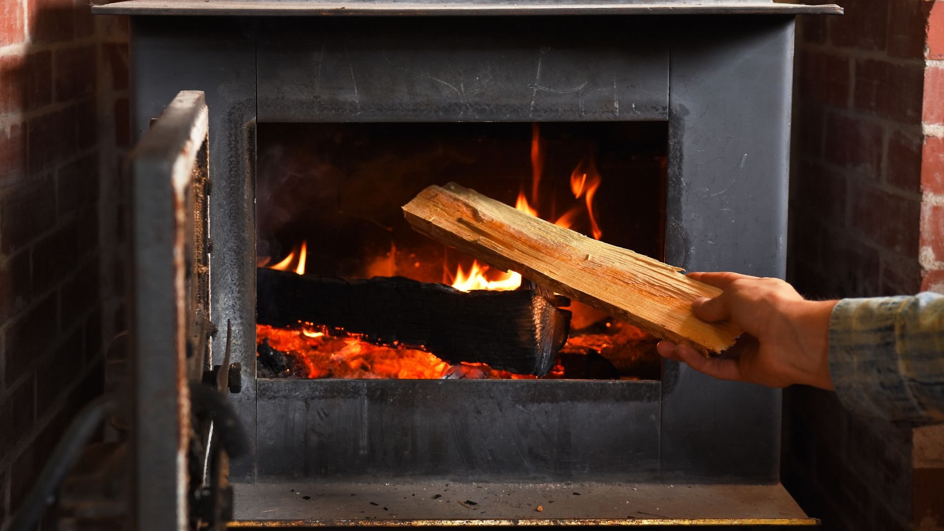 Hand adding wood to a burning fire inside a black metal fireplace