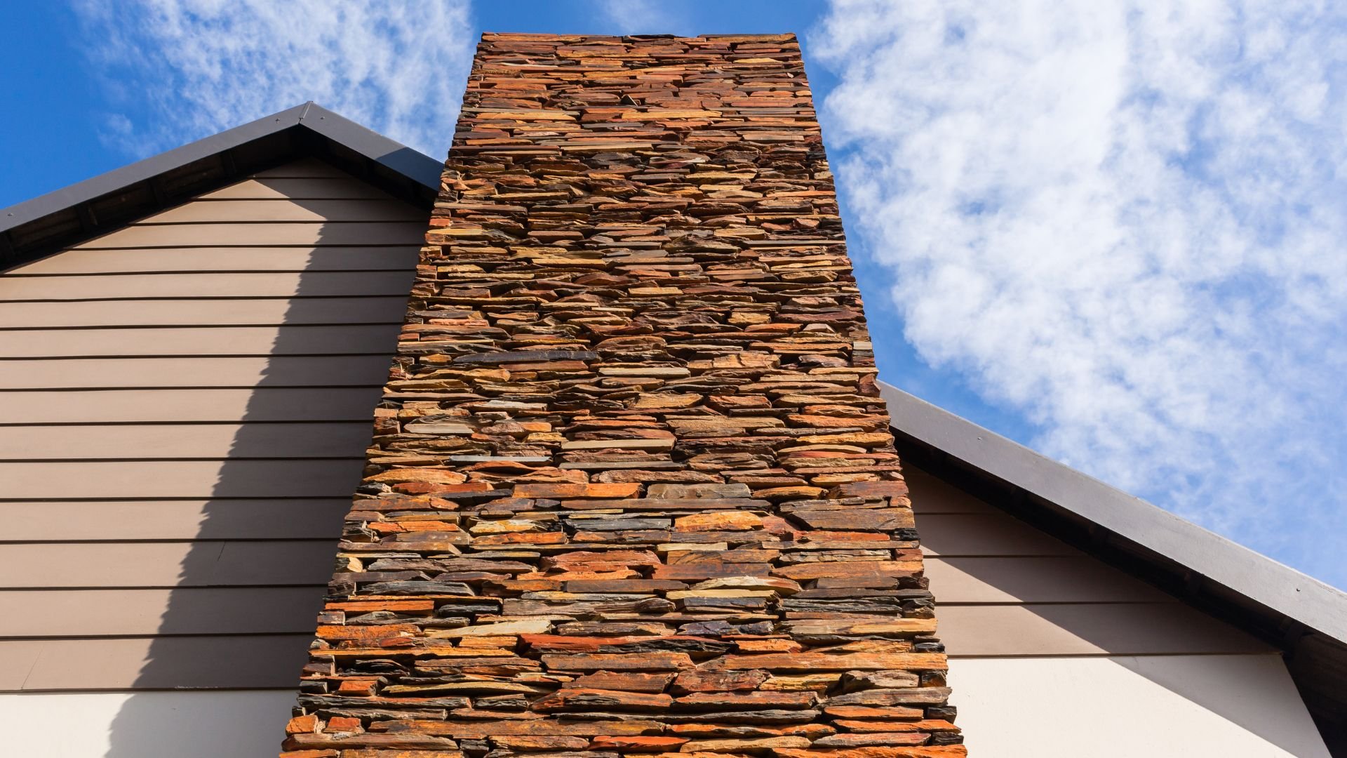 Rustic stone chimney against blue sky and modern house exterior