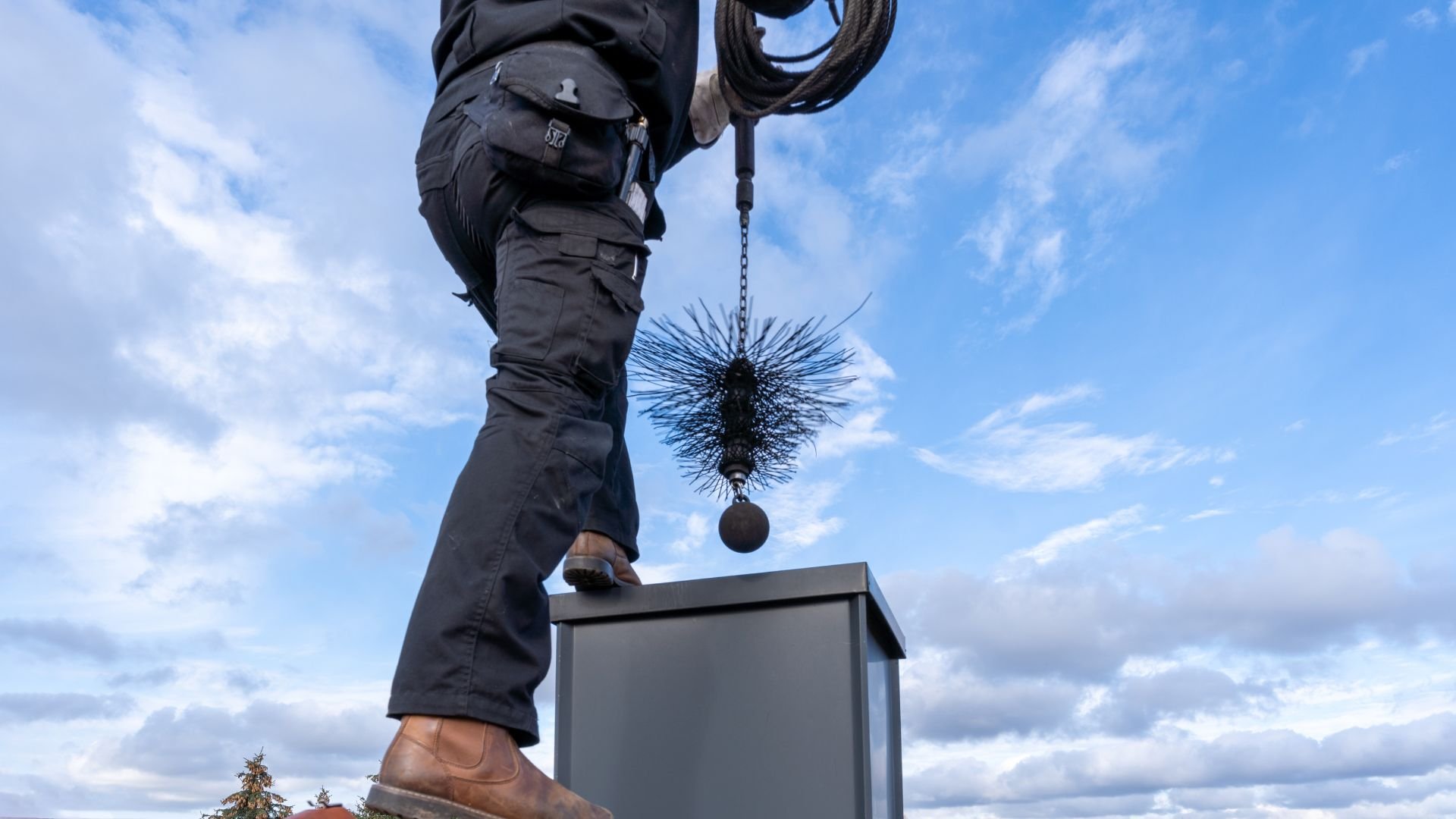 Chimney sweep with brush and rope standing on roof against blue sky