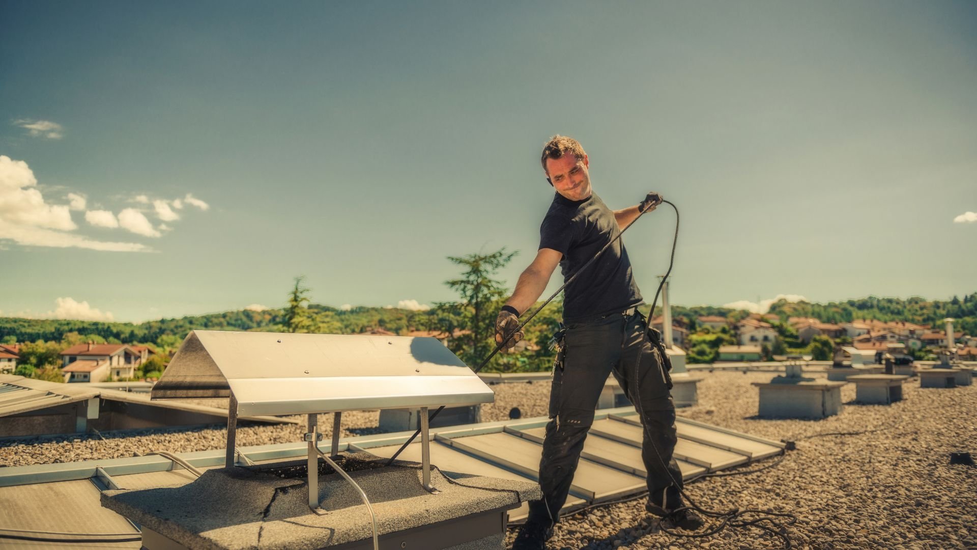 Worker cleaning roof with pressure washer on sunny summer day