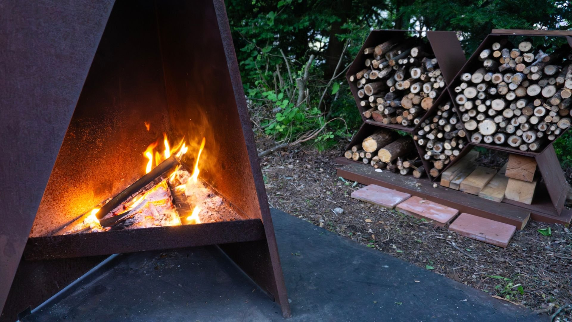 Burning fire in outdoor fireplace with stacked firewood nearby
